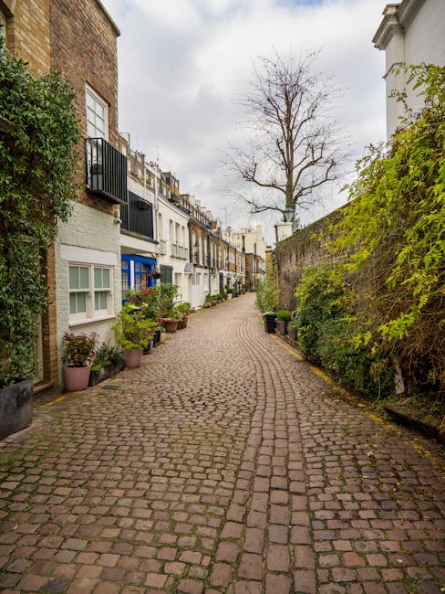 A residential street in South Kensington featuring a row of elegant, multi-story Victorian-style buildings with cream-colored facades and decorative white moldings. The buildings have large sash windo